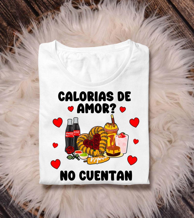 May include: White t-shirt with a graphic design featuring a variety of Mexican foods, including churros, corn on the cob, and Coca-Cola. The text on the shirt reads "Calorias de Amor? No Cuentan".