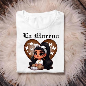 May include: White t-shirt with a brown heart design featuring a cartoon girl with long black hair, a white bandana, and gold hoop earrings. The text "La Morena" is printed above the heart.