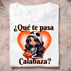May include: A white t-shirt with a black and orange graphic of a skeleton girl holding a pumpkin. The text on the shirt reads "¿Qué te pasa Calabaza?"