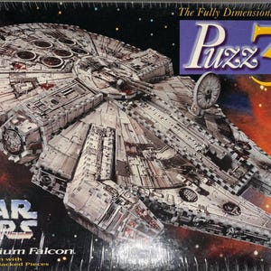 Puede incluir: Una caja de rompecabezas 3D de Star Wars Millennium Falcon. La caja presenta una imagen detallada de la nave espacial contra un fondo espacial. El texto "Puzz 3D" se muestra en la esquina superior derecha.