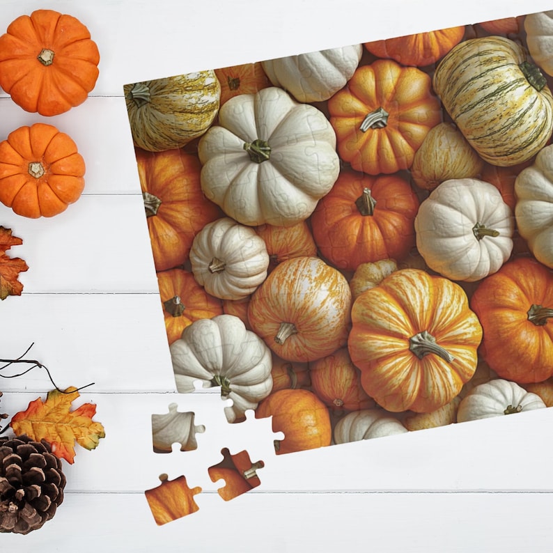 Pode incluir: Um quebra-cabe&ccedil;a com tema de outono, apresentando uma variedade de ab&oacute;boras em tons de laranja, branco e amarelo. As pe&ccedil;as do quebra-cabe&ccedil;a est&atilde;o parcialmente montadas, revelando o design da ab&oacute;bora. A cena &eacute; definida em uma superf&iacute;cie de madeira branca, com ab&oacute;boras e folhas de outono adicionais.