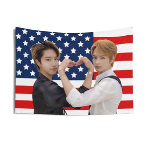 May include: A rectangular tapestry featuring two people forming a heart shape with their hands. The background is the American flag with red and white stripes and a blue field of white stars. The people are wearing black and white outfits.