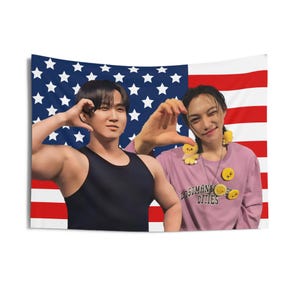 May include: A tapestry featuring an American flag design in the background. Two people are in front of the flag, making heart shapes with their hands. One person wears a black tank top, and the other wears a pink shirt with the text "LOSTMAN CITIES".