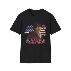 Puede incluir: Camiseta negra con un gráfico de un hombre con una bufanda roja frente a una bandera estadounidense. El texto "S.COUPS SEVENTEEN" está impreso debajo del gráfico.