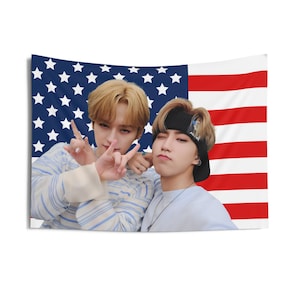 May include: A rectangular wall tapestry featuring a photograph of two people posing in front of an American flag. The flag has red and white stripes and a blue field with white stars. The people are wearing casual clothing.