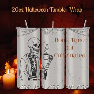 May include: A 20oz Halloween tumbler wrap featuring a skeleton design. The tumbler has a gray background with a spiderweb design at the top and a bone design at the bottom. The text "Bone Tired but Caffeinated" is printed on the tumbler.