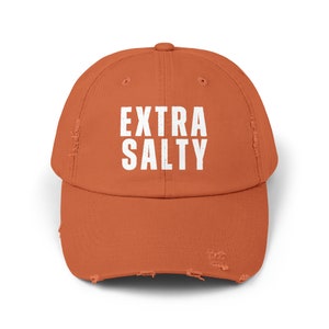 May include: A distressed, burnt orange baseball cap with the text "EXTRA SALTY" in white lettering.