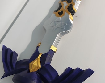 May include: A decorative sword with a silver blade and a hilt featuring a purple and gold design. The handle is wrapped in green and the top of the blade has a black and gold pattern.