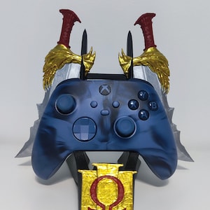 May include: A blue Xbox controller with a marbled design, on a black stand. The stand has a gold emblem with a red symbol, with silver and gold swords. The controller has the Xbox logo.