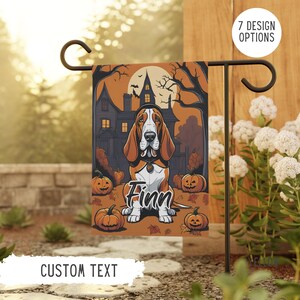 May include: A Halloween garden flag with a Basset Hound in costume, the name "Finn" below. The background shows a haunted house and pumpkins. The flag has the text "CUSTOM TEXT" at the bottom. It is displayed on a black metal stand, perfect for a garden.