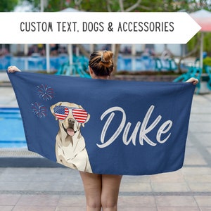 Può includere: Un asciugamano da spiaggia blu con un labrador retriever giallo che indossa occhiali da sole rosso, bianco e blu. Il nome del cane, "Duke", è scritto in bianco sull'asciugamano. Ci sono fuochi d'artificio sullo sfondo.