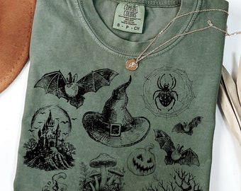 May include: A green t-shirt with a black and white print of various Halloween themed images, including a witch's hat, bats, a spider web, a pumpkin, and a castle. The text "COMFORT COLORS" is visible on the shirt.