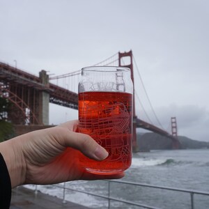 Puede incluir: Una bebida roja en un vaso transparente con un diseño grabado. El puente Golden Gate está en el fondo.