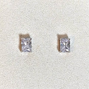 May include: A pair of silver square-shaped stud earrings with clear cubic zirconia stones. The earrings are displayed on a white jewelry display card with the text "La Belle Jewel Boutique".