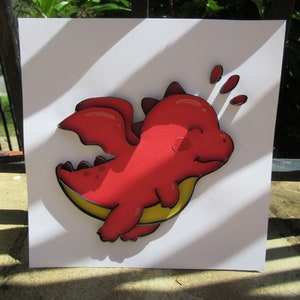 May include: A red paper dragon with yellow wings is flying through the air. The dragon has a happy expression on its face and is surrounded by white paper.