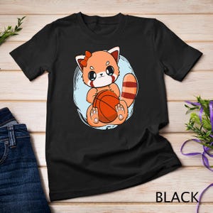 May include: Black t-shirt with a cartoon red panda holding a basketball. The panda has a red bow on its head and is wearing a white shirt.