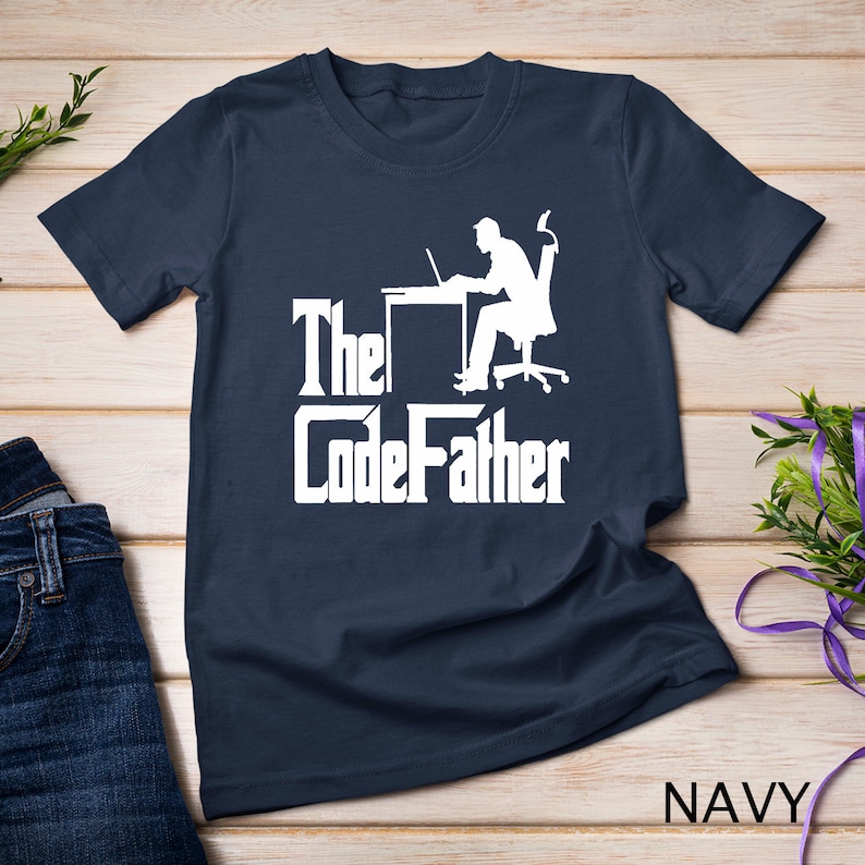 May include: A navy blue t-shirt with a white silhouette of a person sitting at a desk with a laptop. The text "The CodeFather" is printed in white below the silhouette.