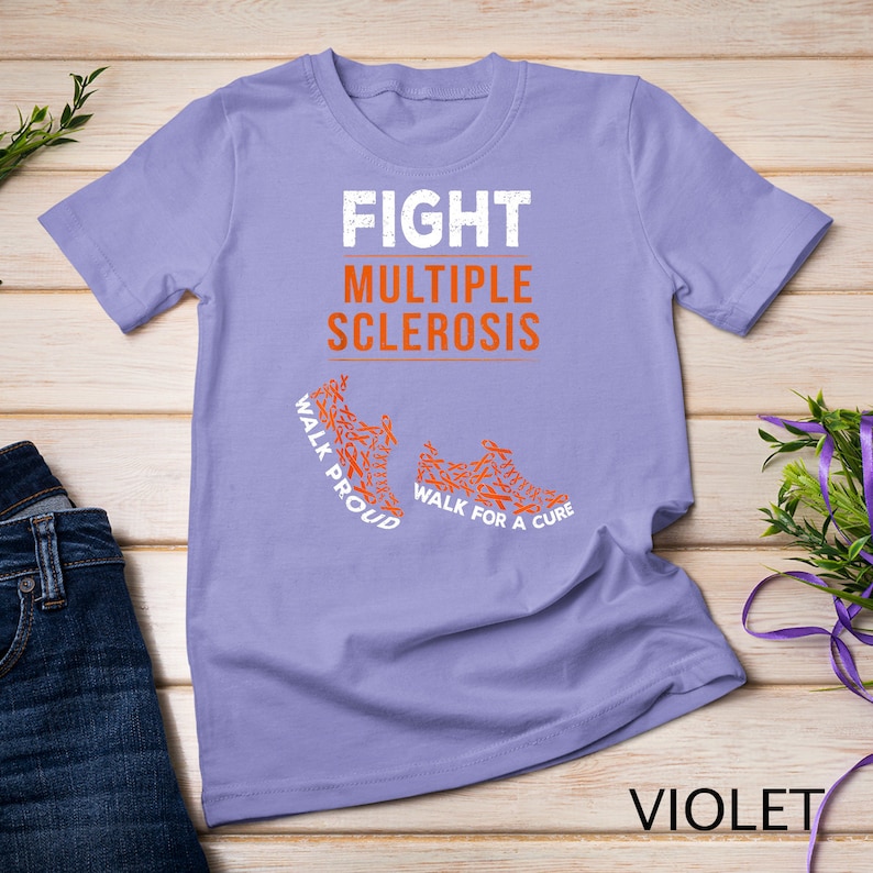 Op de afbeelding: Paars T-shirt met de tekst "FIGHT MULTIPLE SCLEROSIS" in wit. De tekst "WALK PROUD" en "WALK FOR A CURE" staan op het shirt gedrukt met oranje schoencontouren gemaakt van oranje linten.