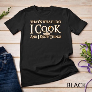 May include: Black t-shirt with the text "That's what I do I cook and I know things" in gold lettering. A small image of a plate with a spatula is above the word "cook".