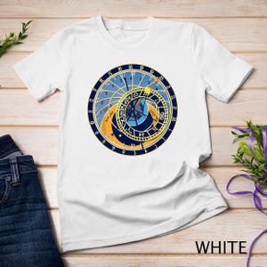 Pode incluir: Camiseta branca com um gráfico do Relógio Astronômico de Praga, um mostrador circular com algarismos romanos e um design azul e dourado.