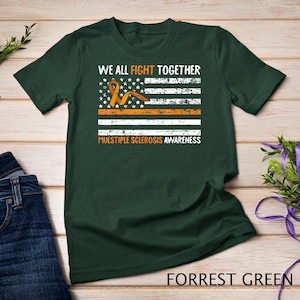 May include: A forest green t-shirt with a distressed American flag design featuring an orange ribbon. The text "We all fight together" and "Multiple Sclerosis Awareness" is printed on the shirt.