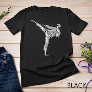 Puede incluir: Camiseta negra con una silueta blanca de una persona en una pose de karate. La silueta está formada por palabras relacionadas con el karate, como "cortesía", "integridad", "autocontrol" y "perseverancia".