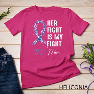 Puede incluir: Camiseta rosa con una cinta azul hecha de corazones y el texto "Her Fight Is My Fight" y "TID Mom".