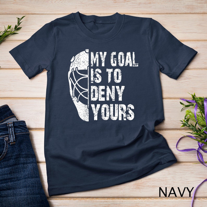 May include: Navy blue t-shirt featuring a white hockey goalie mask and the text "My goal is to deny yours".