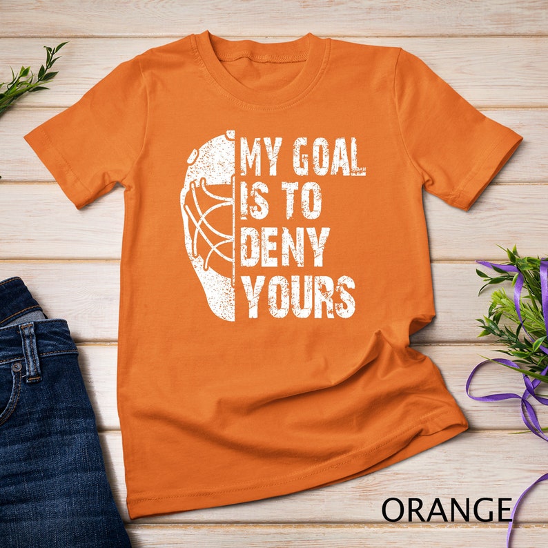 May include: Orange t-shirt with a white hockey goalie mask graphic and the text "My goal is to deny yours".
