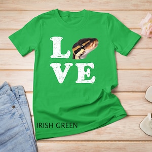 Op de afbeelding: Een groen T-shirt met het woord "LOVE" in witte, verweerde letters. Een slang is opgenomen in de "O" van het woord. De tekst "IRISH GREEN" staat onderaan het shirt gedrukt.