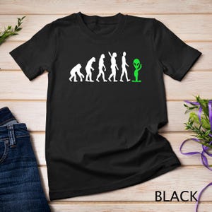 May include: Black t-shirt with a white graphic of the evolution of man, ending with an alien. The text "BLACK" is printed on the bottom right corner of the shirt.