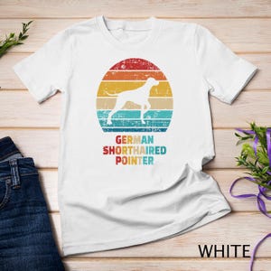 Könnte beinhalten: Weißes T-Shirt mit einer Grafik im Vintage-Stil eines Deutsch Kurzhaar-Hundes vor einem Sonnenuntergang. Der Text "GERMAN SHORTHAIRED POINTER" ist unter der Grafik gedruckt.