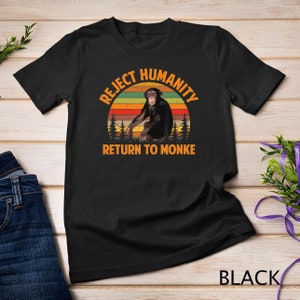 May include: Black t-shirt with a vintage-style graphic of a chimpanzee sitting in front of a sunset. The graphic says "Reject Humanity Return to Monke".