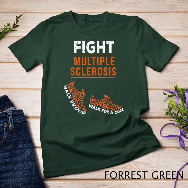 Op de afbeelding: Een donkergroen T-shirt met de tekst "FIGHT MULTIPLE SCLEROSIS" in wit. Het shirt heeft twee oranje schoenafdrukken gemaakt van oranje linten met de tekst "WALK PROUD" en "WALK FOR A CURE".