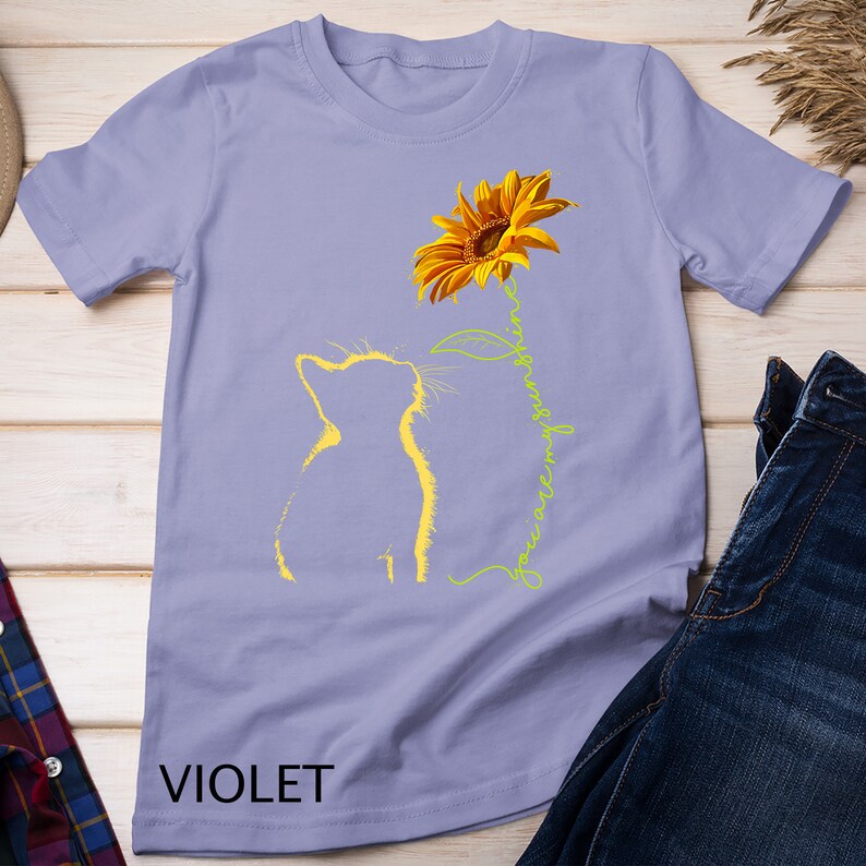 K&ouml;nnte beinhalten: Ein lavendelfarbenes T-Shirt mit einer gelben Katzensilhouette, die zu einer gelben Sonnenblume mit dem Text "You are my sunshine" in Gr&uuml;n schaut.
