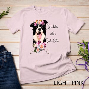 May include: Light pink t-shirt featuring a black and white border collie wearing a flower crown. The shirt has the text "Life is better with a Border Collie" printed on it.