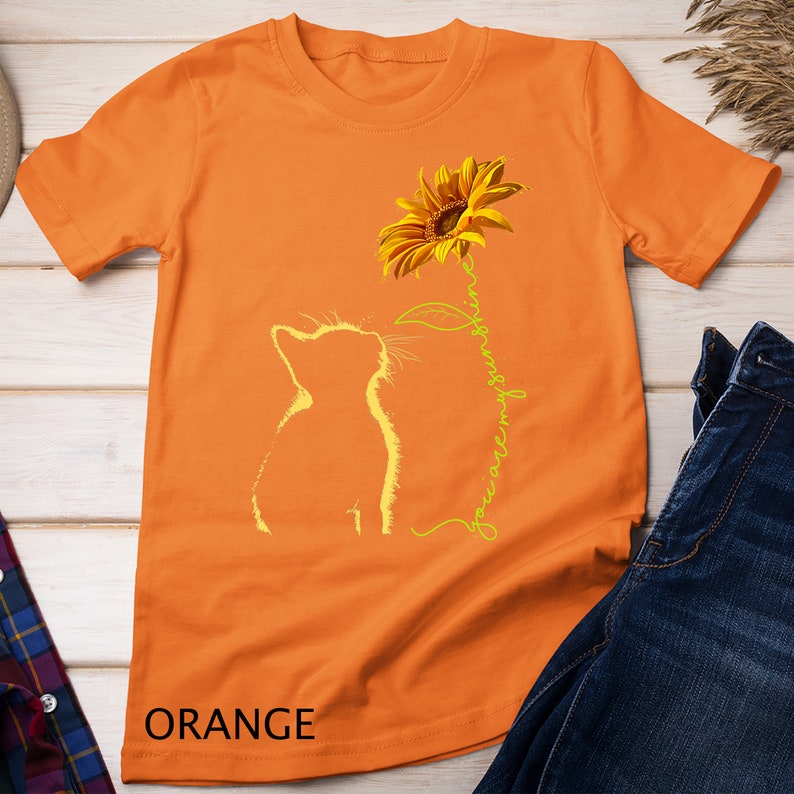K&ouml;nnte beinhalten: Orangefarbenes T-Shirt mit einer Silhouette einer Katze, die zu einer Sonnenblume aufblickt, mit dem Text "You are my sunshine", der entlang des Stiels geschrieben ist.