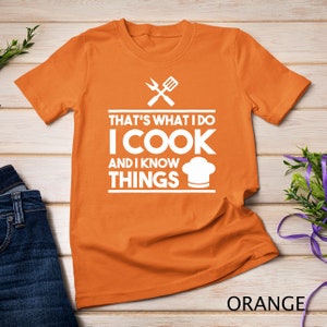 Könnte beinhalten: Orangefarbenes T-Shirt mit weißem Text, der "That's what I do I cook and I know things" lautet, und einem Kochmützen-Motiv.