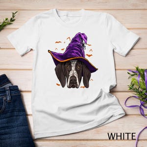 May include: White t-shirt featuring a graphic of a German Shorthaired Pointer wearing a purple witch hat with a spider web and bats. The text "WHITE" is in the bottom right corner of the image.
