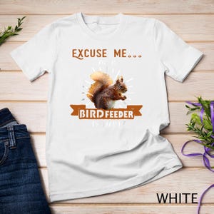 May include: White t-shirt with a brown squirrel graphic and the text "Excuse me... your bird feeder is a bit..." printed on it.