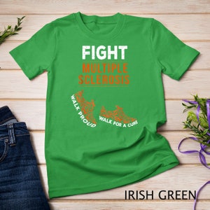 Op de afbeelding: Groen T-shirt met de tekst "FIGHT MULTIPLE SCLEROSIS" in wit. Onder de tekst staan twee oranje voetafdrukken met de tekst "WALK PROUD" en "WALK FOR A CURE". De tekst "IRISH GREEN" staat onderaan de afbeelding.