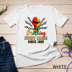 Puede incluir: Camiseta blanca con un puño colorido rompiendo cadenas y el texto "Breaking Every Chain Since 1865".