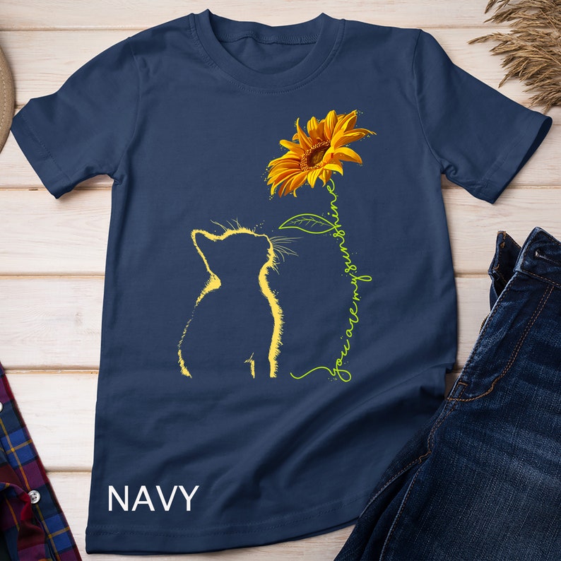 K&ouml;nnte beinhalten: Ein marineblaues T-Shirt mit einer gelben Sonnenblume und einer Silhouette einer Katze, die nach oben schaut. Der Text "You are my sunshine" ist in Gr&uuml;n neben der Sonnenblume geschrieben.