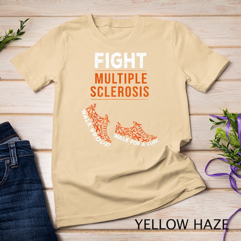 Op de afbeelding: Een beige T-shirt met de tekst "FIGHT MULTIPLE SCLEROSIS" en twee oranje hardloopschoenen gemaakt van oranje bewustzijnslintjes. De tekst op de schoenen luidt "WALK PROUD" en "WALK FOR A CURE".
