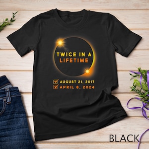 May include: Black t-shirt featuring a graphic of a solar eclipse and the text "Twice in a Lifetime". The dates August 21, 2017 and April 8, 2024 are listed below the graphic.