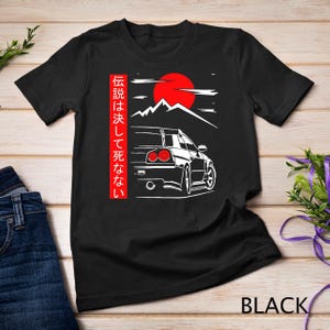 May include: Black t-shirt with a white graphic of a Japanese car, mountains, and a red sun. The text on the shirt reads "伝説は決して死なない".