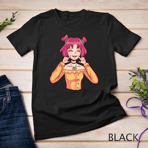 May include: Black t-shirt with a cartoon illustration of a smiling girl with pink hair wearing a yellow shirt and a necklace. The text "BLACK" is printed on the bottom right corner of the shirt.