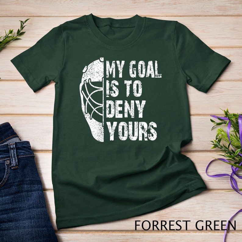 May include: A dark green t-shirt featuring a white hockey goalie mask graphic and the text "My goal is to deny yours".