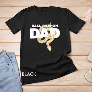 Op de afbeelding: Zwart T-shirt met een witte afbeelding van een koningsboa en de tekst "Ball Python Dad".