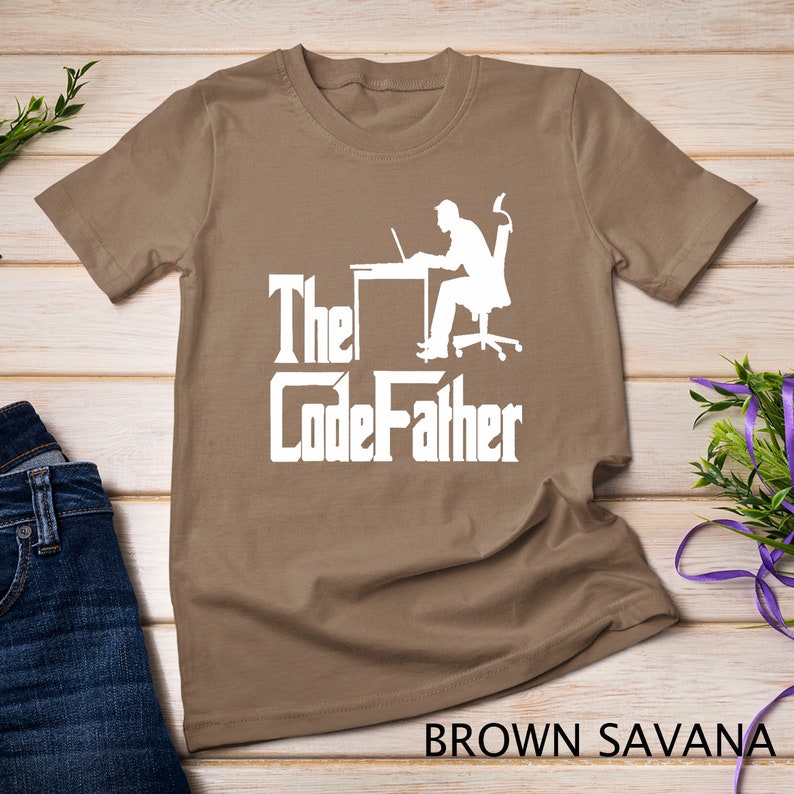 May include: A brown t-shirt with a white silhouette of a person sitting at a desk with a laptop. The text "The CodeFather" is printed in white below the silhouette.